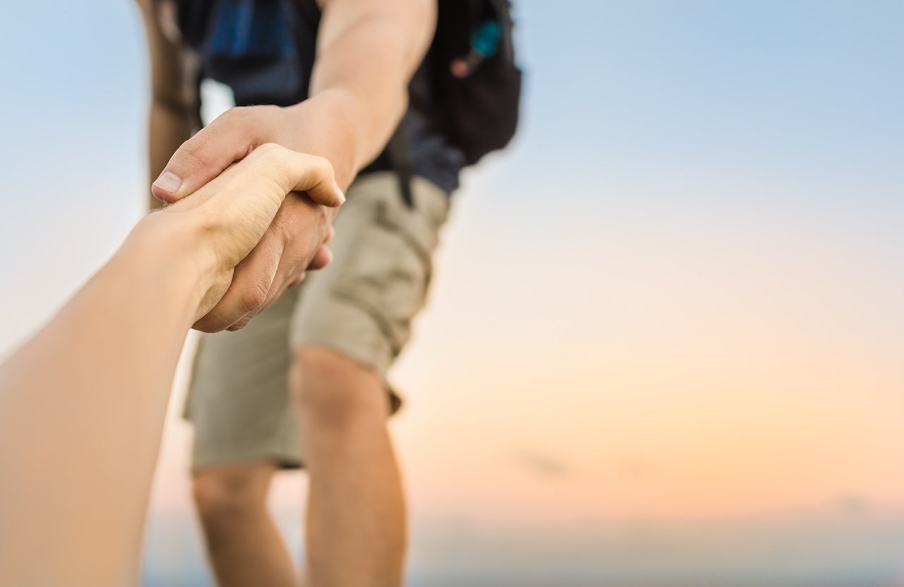 Hikers climbing mountain, helping, giving hand to friend.