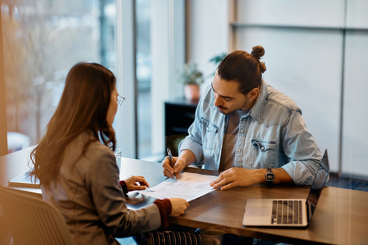 Young Hispanic man signing loan agreement during meeting with his bank manager in office., Young Hispanic man signing loan agreement during meeting with hi Young Hispanic man signing loan agreement during meeting with his bank manager in office., Young Hispanic man signing loan agreement during meeting with hi