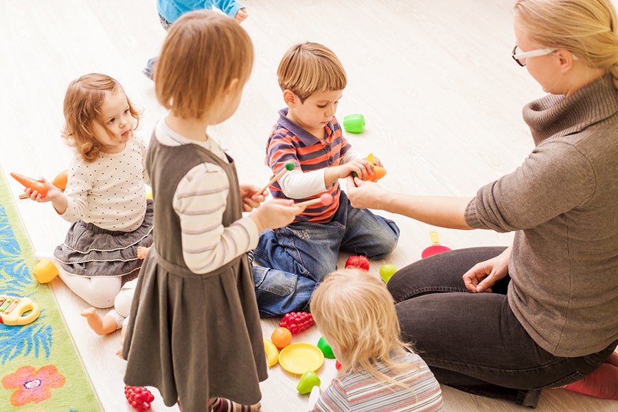 Children with teacher in kindergarten playing cooks