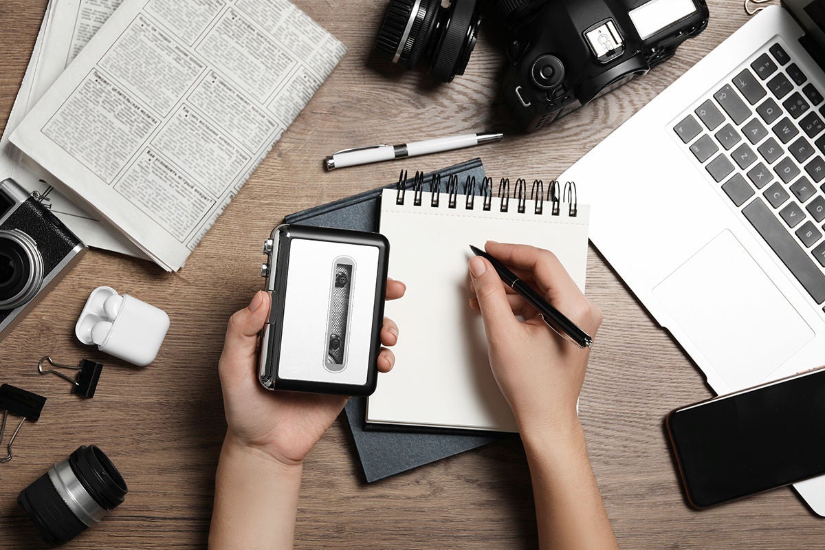 Journalist with voice recorder working at wooden table, top view