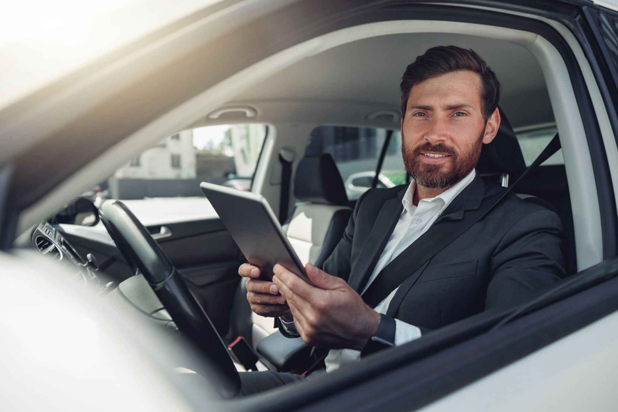 Businessman working on digital tablet while sitting on driver seat in car. Blurred background