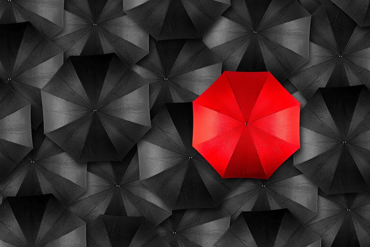 roter Regenschirm inmitten schwarzer Regenschirme