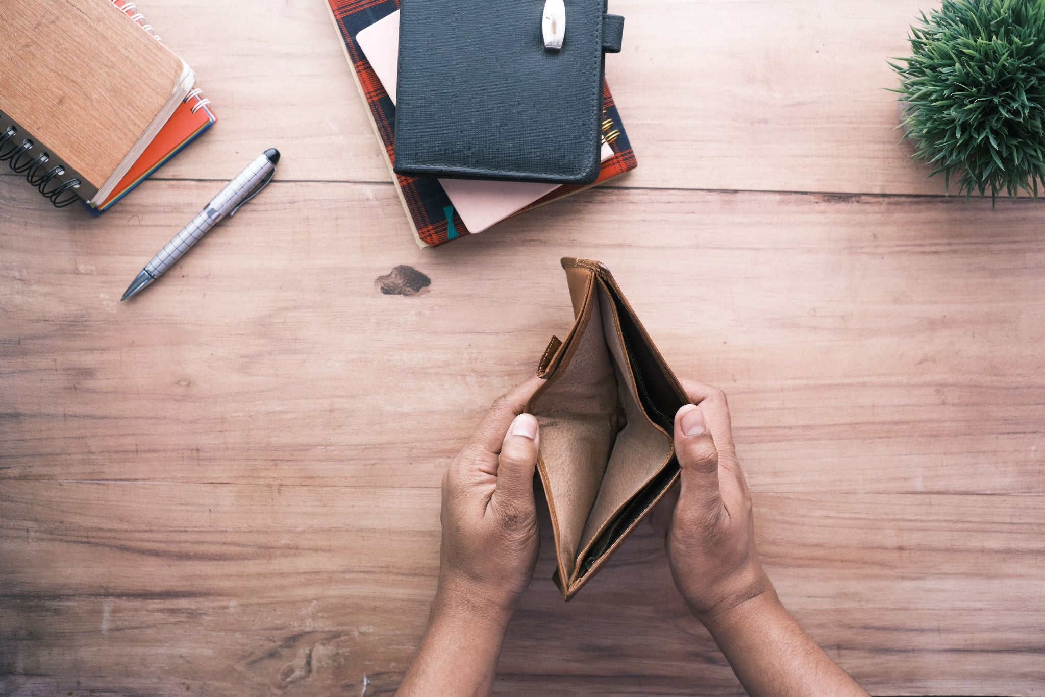 Hände, die eine leere Brieftasche halten, sind vor dem Hintergrund eines braunen Holztisches zu sehen