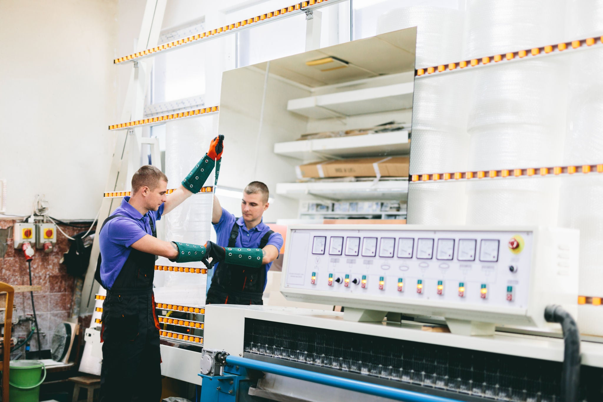 Glazier worker operates mirror glass cutting machine in workshop