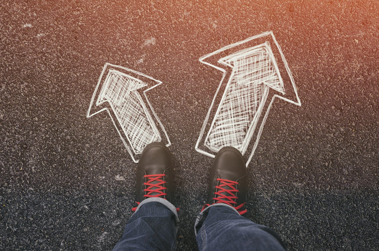 Sneakers on the asphalt road with drawn arrows pointing in two directions. Making decisions and making choices concept.