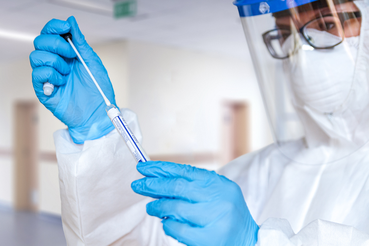 Corona Test Frau im Schutzanzug mit Coronatest